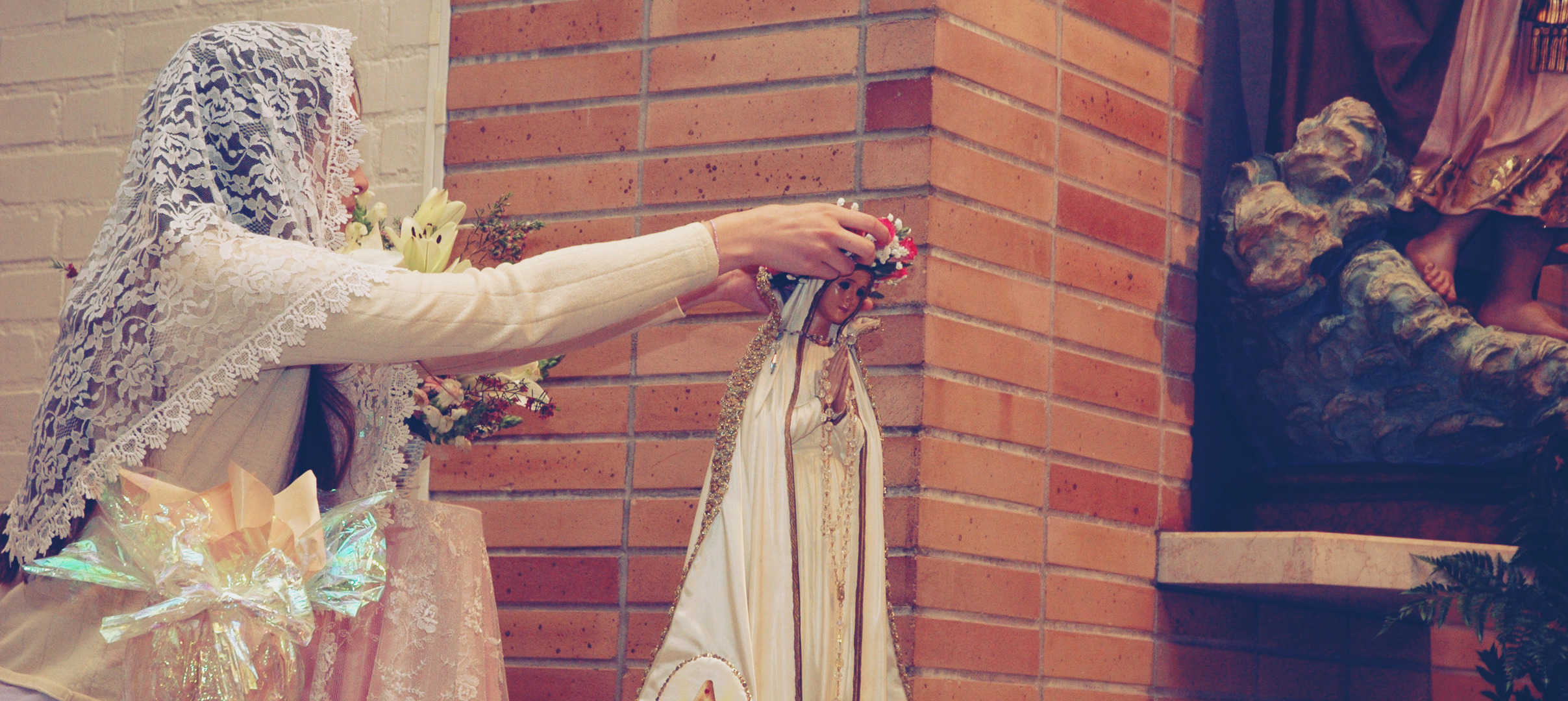 Lay playing a flower crown on statue of Mary
