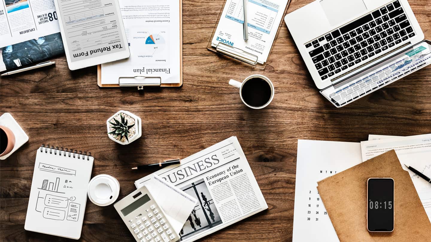 Desk covered with computer, coffee, office supplies and papers