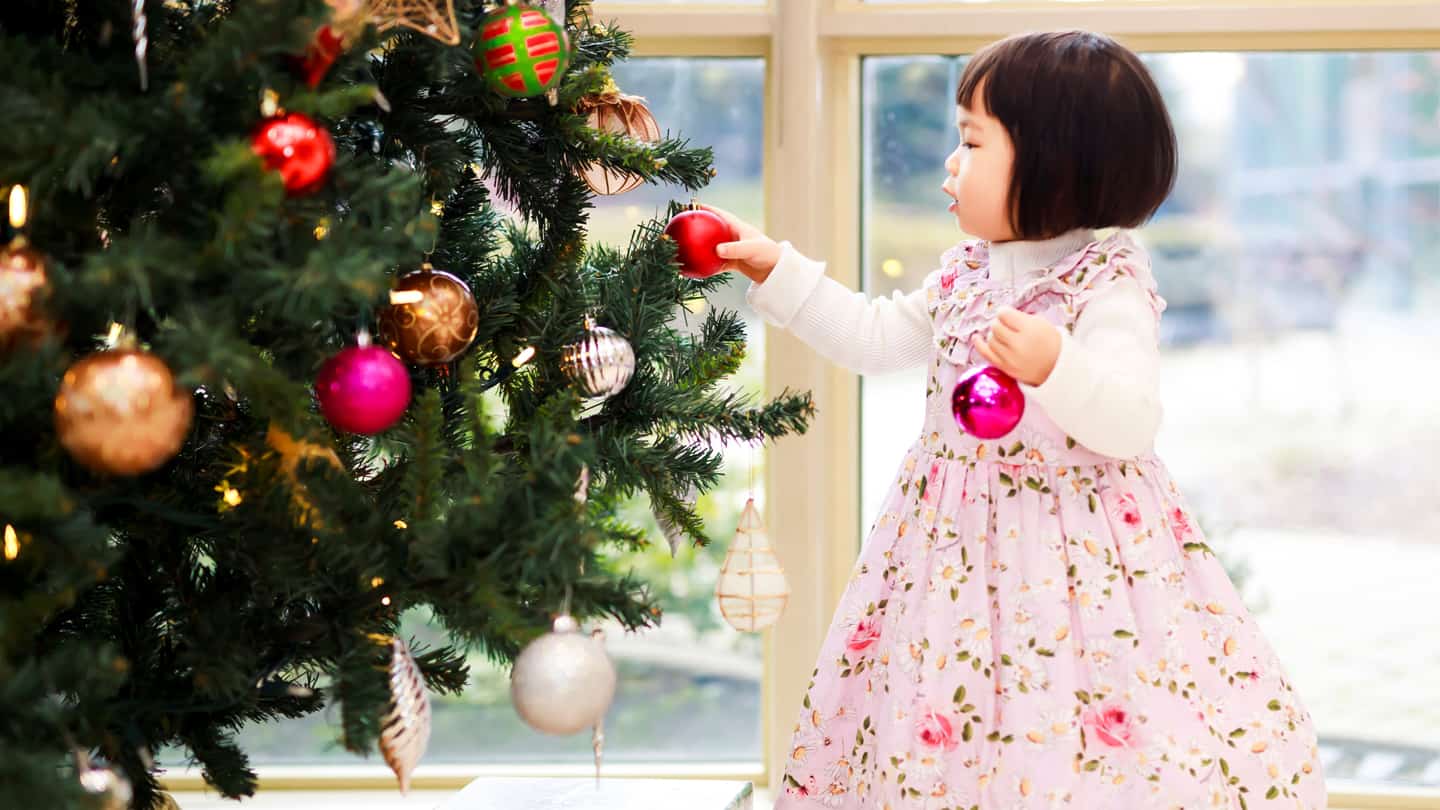 child hanging Christmas tree ornaments