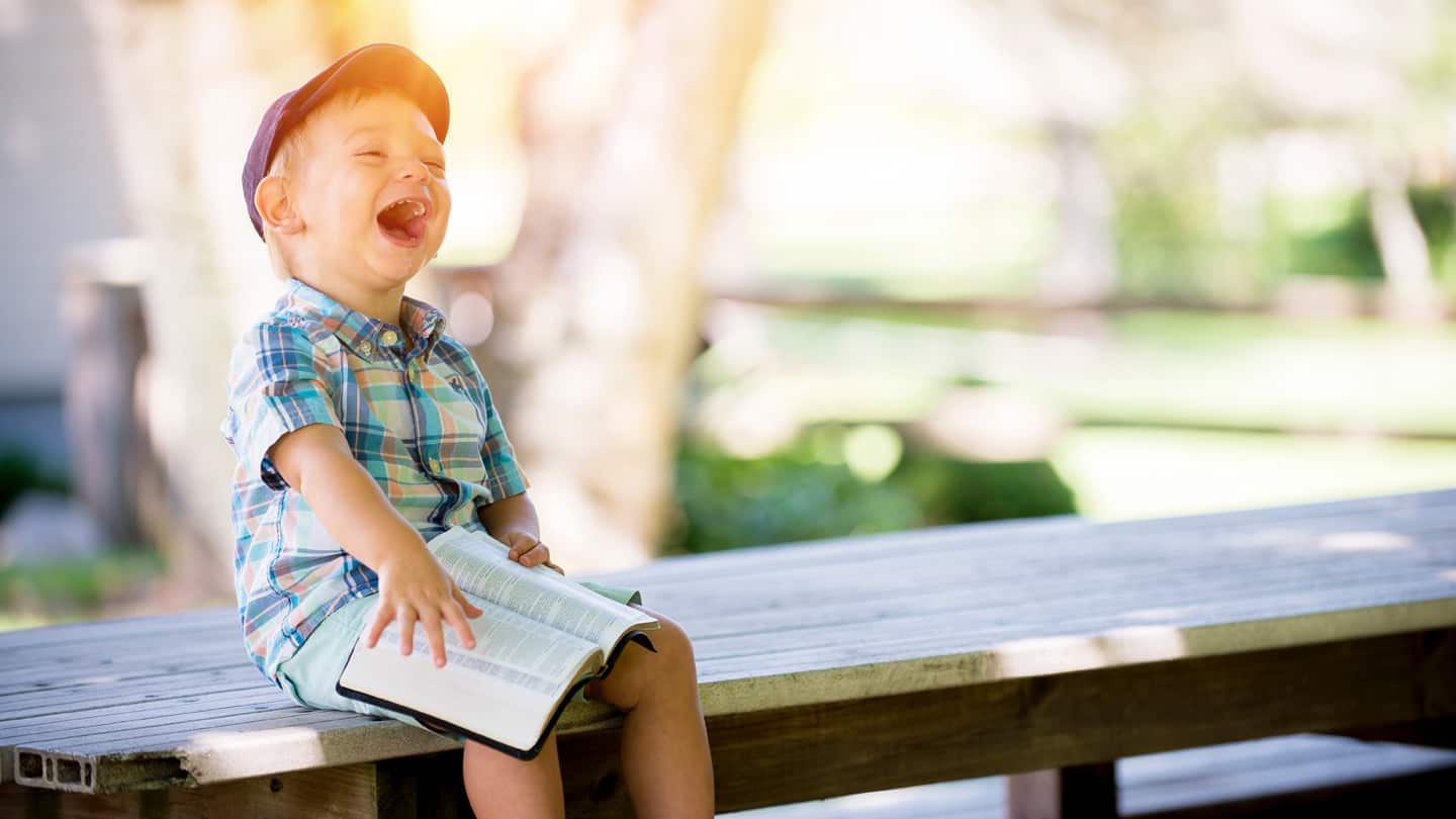 practical Tips_1440 child laughing. sitting on bench, with bible on lap