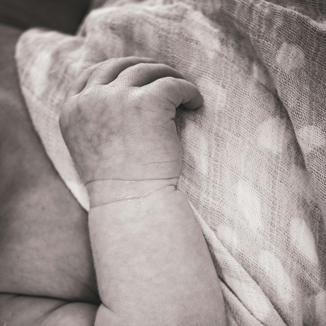 A baby's hand clasping a blanket.