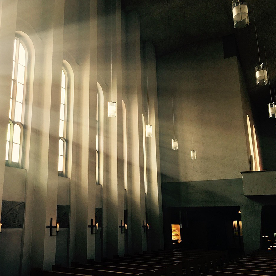 Light streams in from large windows in the side of a darkly-lit church.