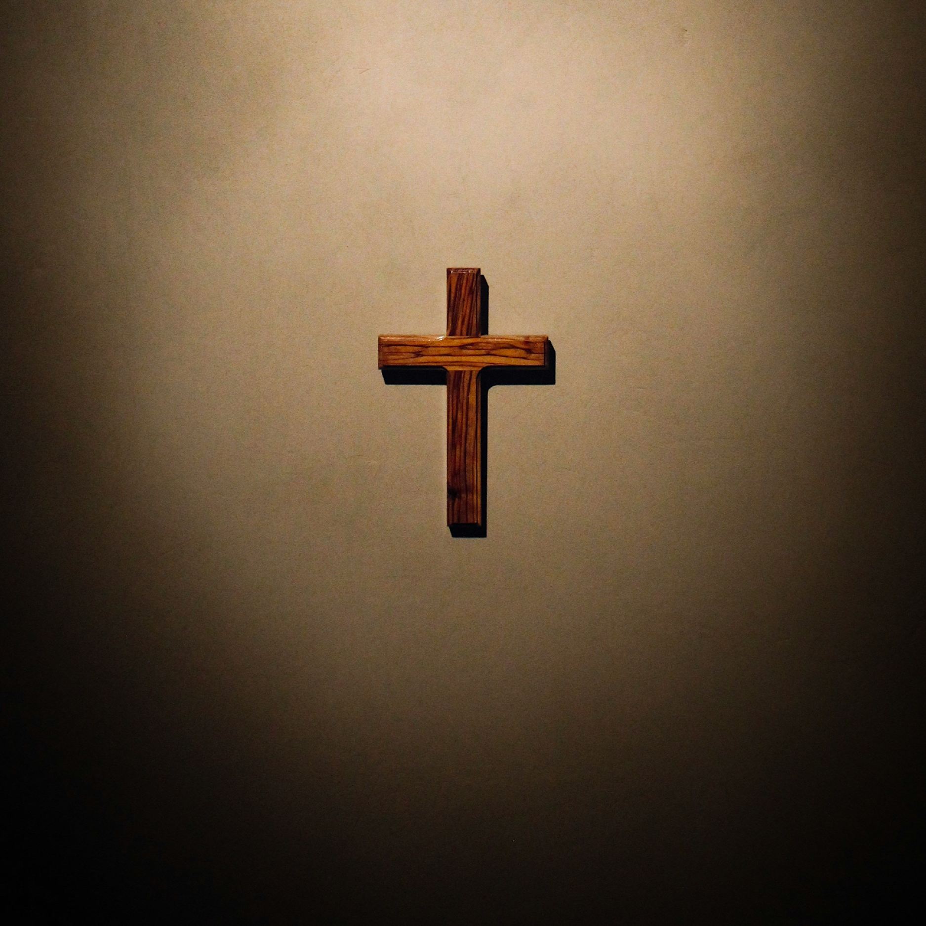 Wooden cross spotlighted against a white wall.