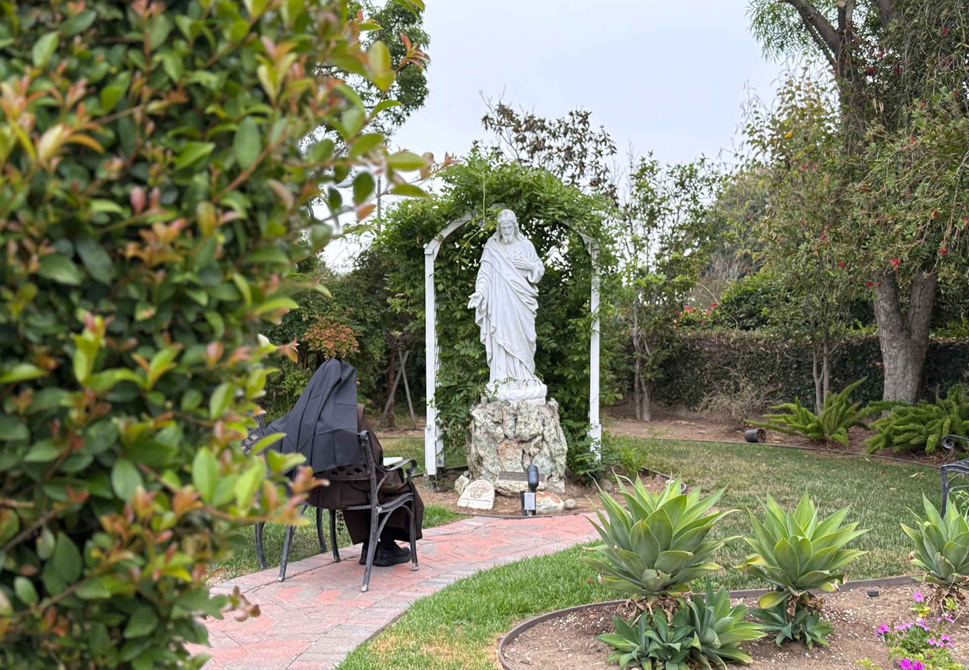 Sister sitting before a statue of the Sacred Heart of Jesus with a prayer book open in her lap.