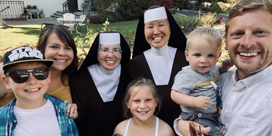 Two Carmelite Sisters standing with a visiting family. All are smiling.