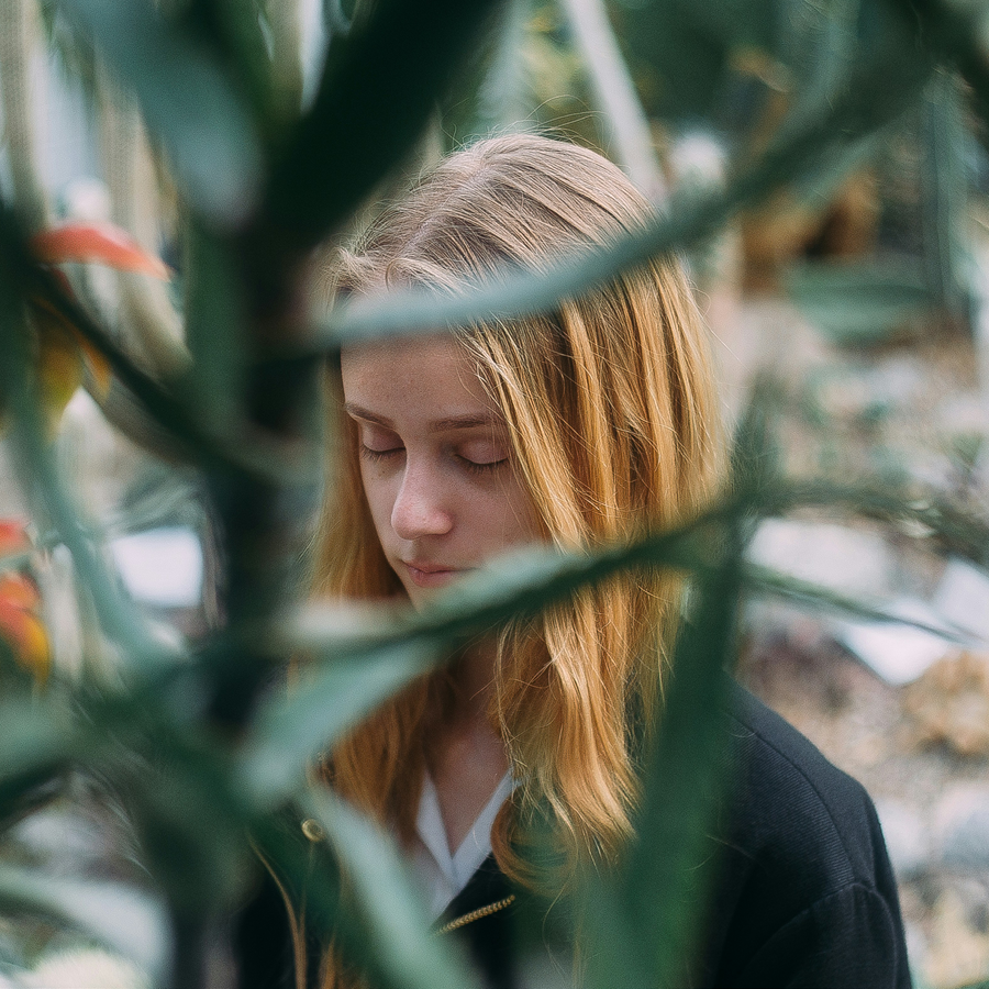 Woman with eyes closed in prayer, out of focus plant stalks slightly blocking her face.