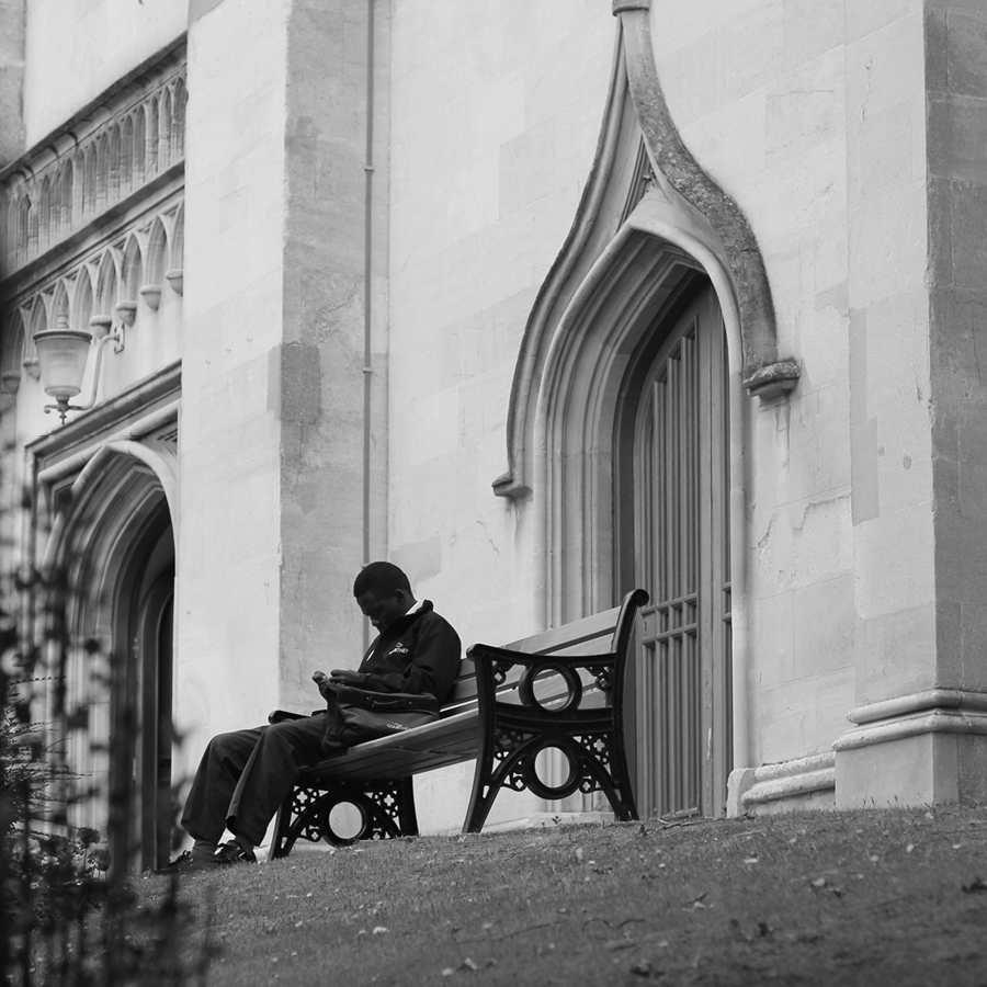Man sitting on bench outside of church in black and white.