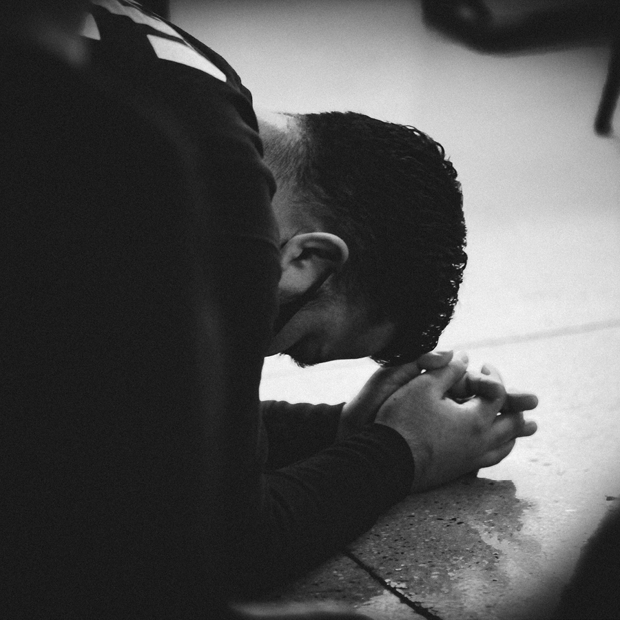 Man bowing head in prayer, forehead almost touching the ground.