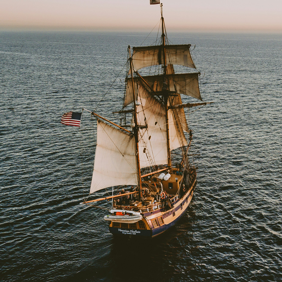 Ship with sails on the ocean sailing toward a hazy horizon.