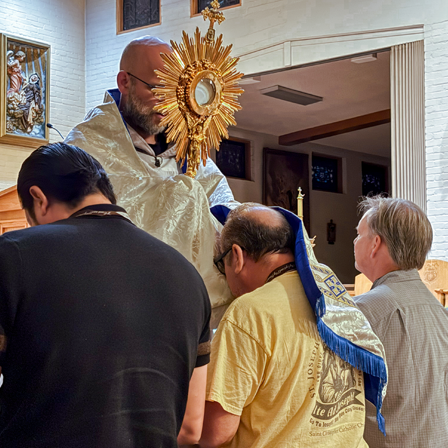 Three men kneeling before a priest holding a monstrance over them.