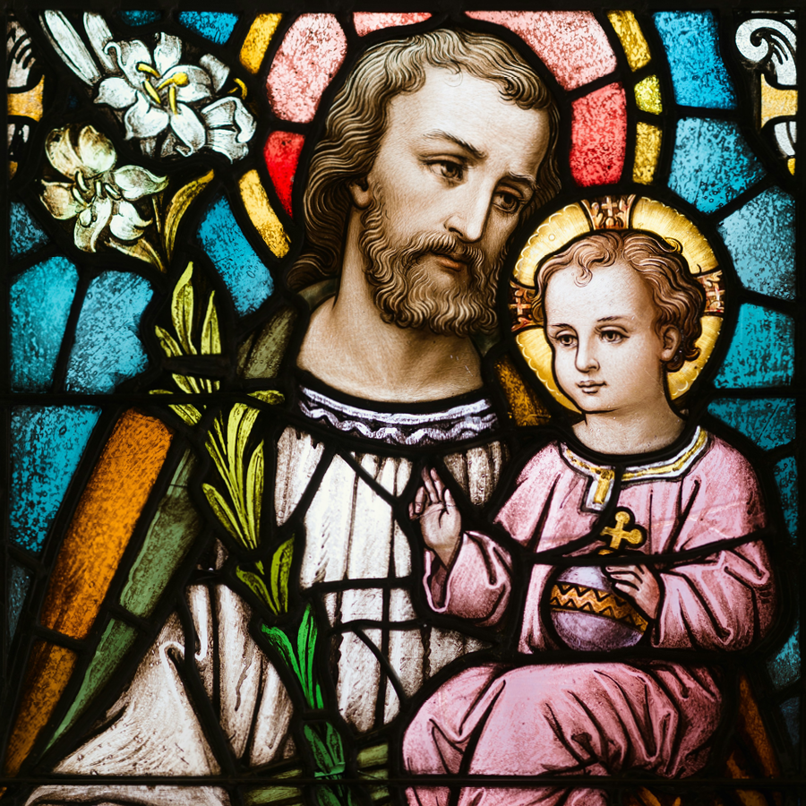 Stained glass of St. Joseph holding the child Jesus in his arms.
