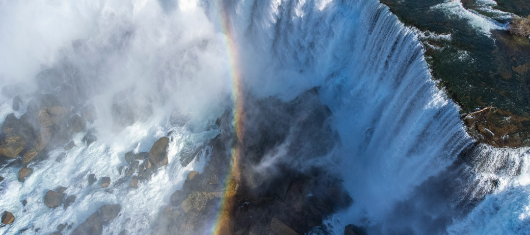 A rainbow over a waterfall crashing down onto the rocks below.