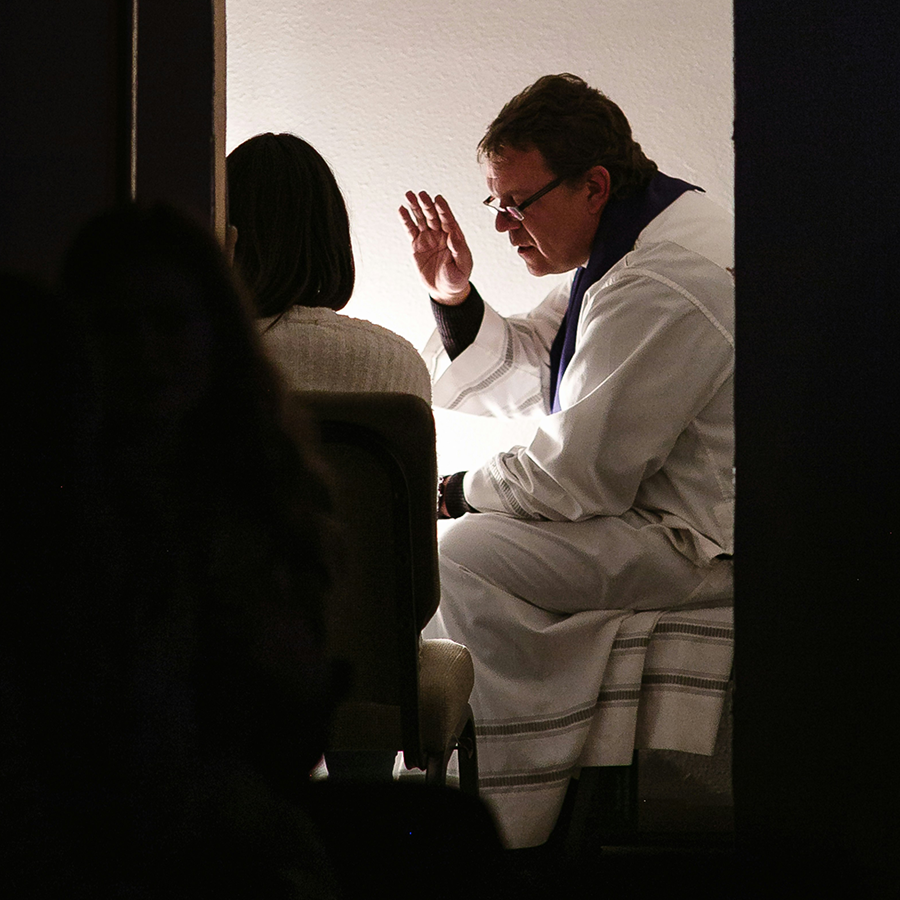 A priest raises his right hand in blessing over a lay person with their head bowed.